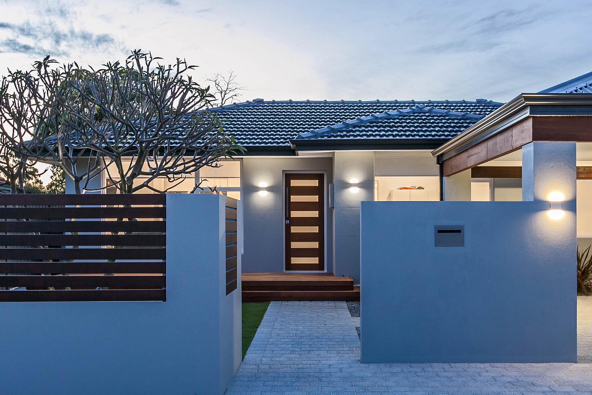 Street frontage at dusk, with a rendered privacy wall and a lit timber entry door