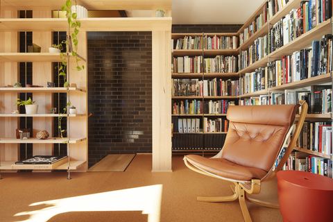 A double-height study lined floor to ceiling with bookshelves, a leather lounge chair by the window