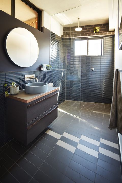 Bathroom finished in dark tile, with a round mirror above a concrete basin on a timber vanity