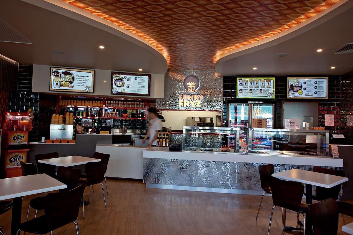 Servery counter beneath an illuminated Funky Fryz sign, its front tiled in silver mosaic under a curved backlit ceiling