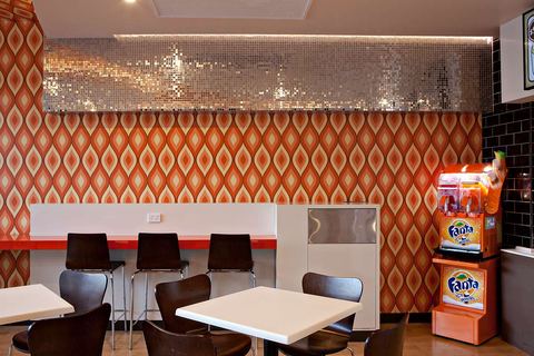 Bar seating along a red-edged bench, against retro orange wallpaper under a band of silver mosaic tile