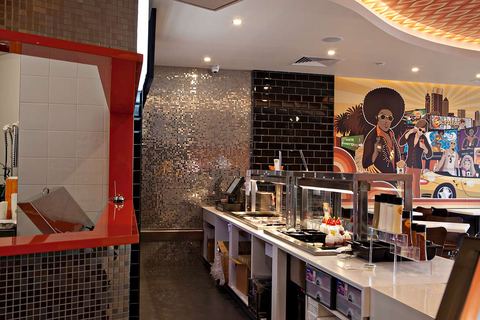 Stainless hot-food line the length of the servery, backed by black subway tile and silver mosaic
