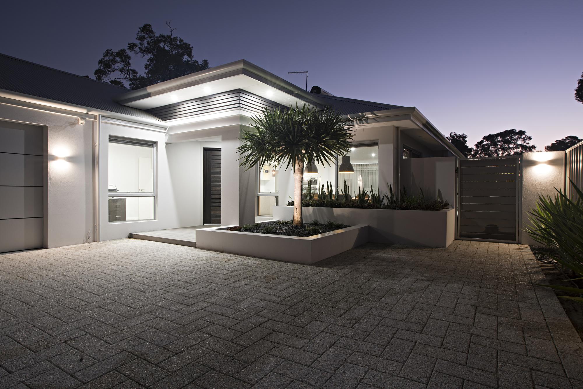 Paved entry courtyard at dusk, lit under a wide eave with a raised planter