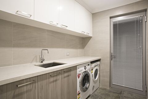 Laundry with a full-length benchtop, overhead cabinetry and a louvred door