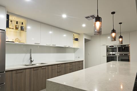 Kitchen with a stone island, white overheads and pendant lights