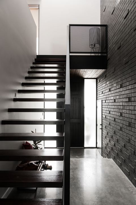 Black steel open-tread stair rising against a grey brick wall