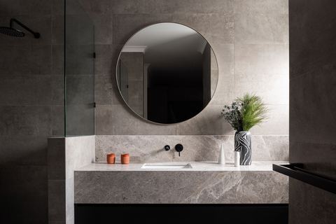 Bathroom in grey stone, with a round mirror and wall-mounted tapware