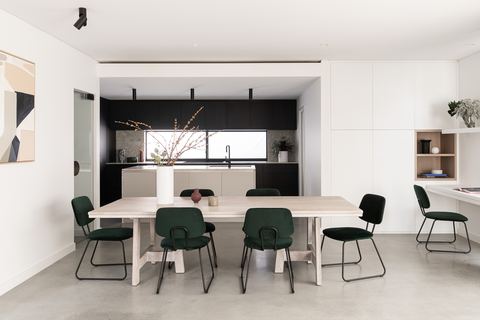 Dining table and kitchen beyond, in white joinery with a black splashback