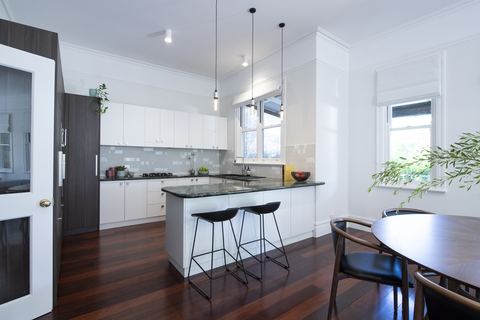 White kitchen with a stone island, pendant lights and jarrah floors